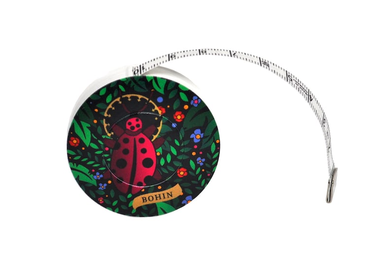 K&ouml;nnte beinhalten: Ein wei&szlig;es Ma&szlig;band mit einem Marienk&auml;fer-Design. Der Marienk&auml;fer ist rot mit schwarzen Punkten und von gr&uuml;nen Bl&auml;ttern und Blumen umgeben. Das Ma&szlig;band ist mit "BOHIN" beschriftet.