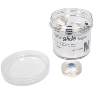 May include: A clear plastic container with a white lid filled with white thread spools. The container has the text "magna-glide delights" and "The perfect match to Glide top thread." The container also has the text "Lot 11121AF" and "M JUMBO".