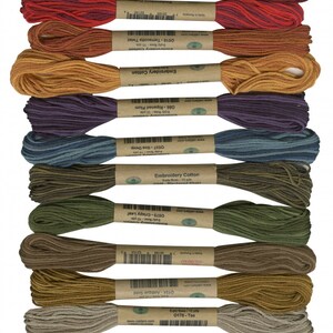 May include: Ten spools of embroidery floss in various shades of red, orange, purple, blue, green, brown, gold, and beige. Each spool is labeled with the color name and the brand "Valdani Embroidery Cotton".
