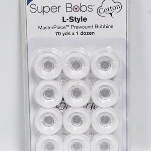 May include: A pack of 12 white plastic bobbins for sewing machines. The pack is labelled "Super Bobs Cotton L-Style MasterPiece Prewound Bobbins 70 yds x 1 dozen".
