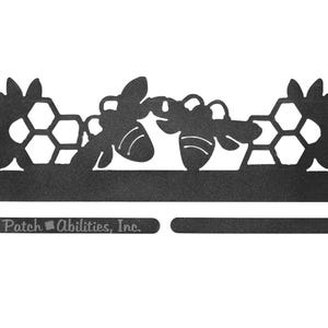 May include: Black metal bee-themed decorative item. The design features two bees, honeycomb shapes, and flower accents. The text "Patch Abilities, Inc." is visible on the bottom. This item is likely for home decor.