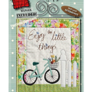 Op de afbeelding: Een kleurrijk quiltpatroon met een fiets met een mand vol bloemen, een wit hek en de tekst "Enjoy the little things". De quilt is 30,5 cm bij 35,6 cm en maakt deel uit van een serie genaamd "Patch Abilities, Inc."