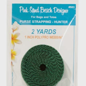 May include: A roll of hunter green polypro webbing for bags and totes, packaged in a clear plastic bag. The label reads Pink Sand Beach Designs #503, 2 YARDS, 1 INCH POLYPRO WEBBING, and PURSE STRAPPING - HUNTER, with white and yellow flower graphics.