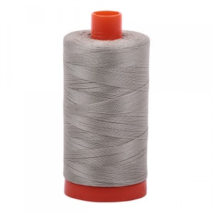 Puede incluir: Una bobina de hilo de coser gris con una bobina de plástico naranja.
