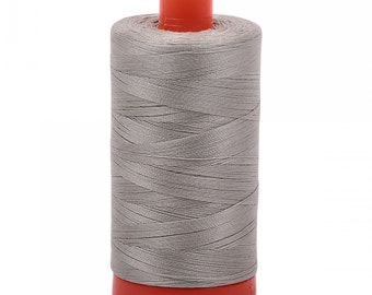 Puede incluir: Una bobina de hilo de coser gris con una bobina de plástico naranja.