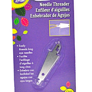 Puede incluir: Un enhebrador de agujas plateado empaquetado en una tarjeta morada con el texto "Needle Threader, Enfileur d'aiguilles, Enhebrador de Agujas" y "1 ct".