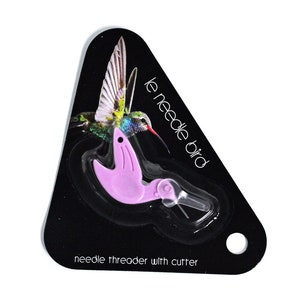 Könnte beinhalten: Ein rosa Plastik-Nadelfäder mit einem Cutter, geformt wie ein Kolibri. Die Verpackung ist schwarz mit dem Text "le needle bird" und "needle threader with cutter".