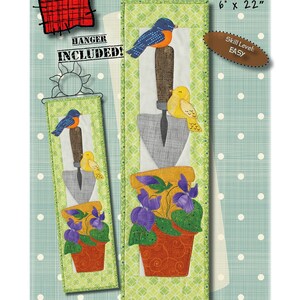 Könnte beinhalten: Ein Quiltmuster für eine Wandbehänge mit einem Vogel, einer Kelle und einem Topf mit violetten Blumen. Das Muster trägt den Titel "Birds 'n Spring Violets" und ist 15,2 cm x 55,9 cm groß. Das Muster ist als "Einfach" gekennzeichnet und beinhaltet einen Aufhänger.