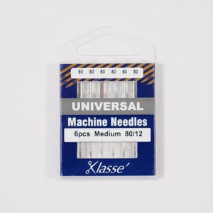 May include: A pack of six Klasse universal machine needles in a blue and white plastic case. The packaging displays the text Universal Machine Needles, 6pcs Medium 80/12, and Klasse. The needles are visible through a clear window in the center.