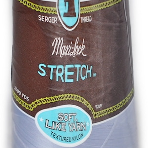 Peut inclure: Une bobine de fil à coudre Maxi-Lock Stretch de couleur bleu clair. La bobine est étiquetée "Maxi-Lock Stretch" et "Soft, Like Yarn, Textured Nylon". Elle mesure 2000 yards (1828 mètres).