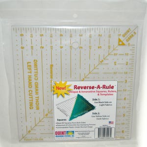 May include: A clear plastic square quilting ruler with yellow grid markings and measurements in inches. The tool features text including Reverse-A-Rule, Left Hand Cutting, and Right Hand Cutting. It is packaged in a clear plastic bag with a product label.