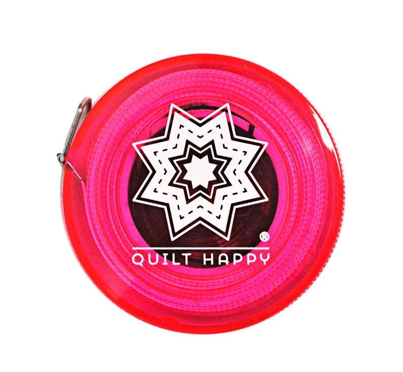 Puede incluir: Un flex&oacute;metro rosa y rojo con el texto "QUILT HAPPY" y un dise&ntilde;o de estrella blanca. El flex&oacute;metro es redondo y tiene un clip de metal.