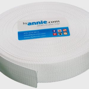 May include: A roll of white woven webbing tape featuring a textured surface. A rectangular white and blue label is placed on top, displaying the text byannie.com, what's in your bag?, 435-674-9816, info@ByAnnie.com, and www.ByAnnie.com.