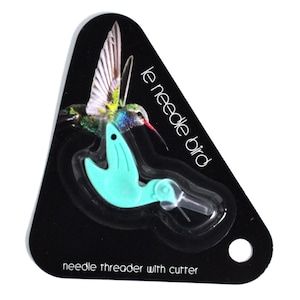 Könnte beinhalten: Ein türkisfarbener Nadelfäder in Form eines Kolibris mit einem Schneidewerkzeug. Der Nadelfäder ist auf einer schwarzen Karte verpackt mit dem Text "le needle bird" und "needle threader with cutter".