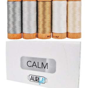 Pode incluir: Um conjunto de quatro carretéis de fio Aurifil na paleta de cores "Calm". Os carretéis são envoltos em bobinas de madeira e têm o logotipo Aurifil e a inscrição "Made in Italy".