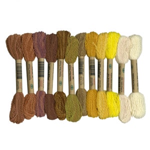 Può includere: Un set di 10 bobine di filo di lana Valdani in diverse tonalità di marrone, giallo e bianco. Il filo è avvolto attorno a bobine di cartone con etichette che recitano "Valdani Wool Thread".