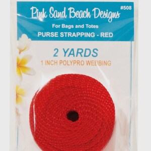 May include: A roll of red polypro webbing for bags and totes, packaged in a clear plastic bag. The label reads Pink Sand Beach Designs #508, 2 YARDS, 1 INCH POLYPRO WEBBING. The red strapping is coiled into a circular shape with a center hole.
