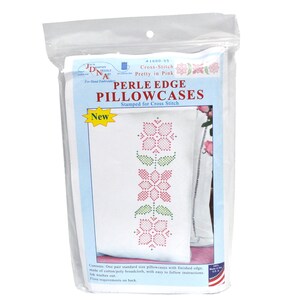 Peut inclure: Un paquet de taies d'oreiller en coton blanc avec un motif floral rose et vert estampé pour point de croix. Le paquet indique "Perle Edge Pillowcases" et "Pretty in Pink".