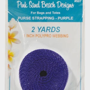 May include: A roll of purple polypro webbing for bags and totes in clear packaging. The label reads Pink Sand Beach Designs #507, PURSE STRAPPING - PURPLE, 2 YARDS, 1 INCH POLYPRO WEBBING. The packaging features white and yellow flower graphics.