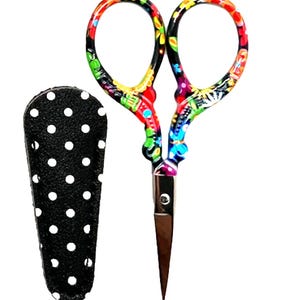 May include: Colorful floral embroidery scissors with a black and white polka dot sheath. The scissors have a silver blade and a vibrant design of flowers and leaves in red, yellow, blue, and green. The sheath is black with white polka dots.