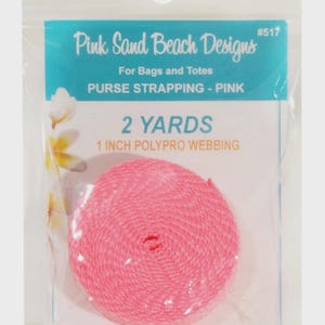 May include: A roll of pink polypro webbing for bags and totes, packaged in a clear plastic bag. The label reads Pink Sand Beach Designs #517, 2 YARDS, 1 INCH POLYPRO WEBBING, PURSE STRAPPING - PINK, and www.pinksandbeachdesigns.com.
