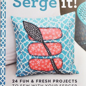 May include: A book titled Serge it! 24 Fun & Fresh Projects to Sew with Your Serger by Jenny Doh & Cynthia Shaffer. The cover features a square throw pillow with a blue and white geometric pattern, three coral floral patches, and a black oar.