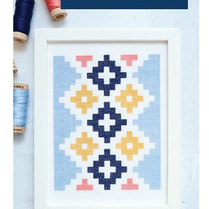 May include: A framed cross stitch pattern with a geometric design in blue, yellow, pink, and white. The pattern is titled "ANDES ODE" and is described as a "quilt inspired cross stitch pattern".