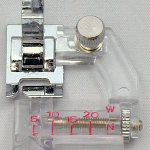 May include: A silver sewing machine foot with a clear plastic adjustable guide. The guide has markings for 5, 10, 15, 20, W, and N.