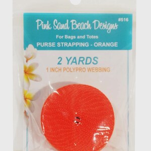 May include: A roll of bright orange polypro webbing for bags and totes, packaged in a clear plastic bag. The label reads Pink Sand Beach Designs #516, 2 YARDS, 1 INCH POLYPRO WEBBING, and PURSE STRAPPING - ORANGE, with white flower graphics.
