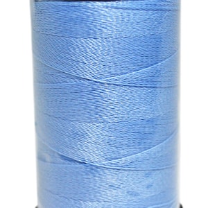 May include: A spool of light blue thread in a clear plastic container with a black lid.