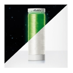 May include: A spool of Mettler sewing thread featuring a dual-tone appearance. The top half of the thread glows in a vibrant green, while the bottom half appears as a neutral white. The spool has a white cap with the brand name Mettler printed on it.