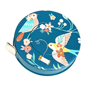 May include: A teal, round tape measure with a decorative bird and floral design. The tape measure features a metal pull tab and a detailed illustration of two birds, flowers, and a spool of thread. The design is printed on the top of the tape measure.
