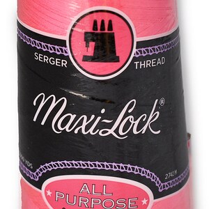 Op de afbeelding: Een roze spoel Maxi-Lock All Purpose Spun Polyester Serger Thread. De spoel heeft een zwart label met witte tekst die "Maxi-Lock" en "All Purpose Spun Polyester" zegt.