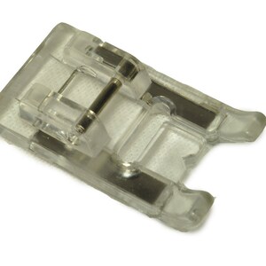May include: A clear plastic sewing machine foot with a metal bar.