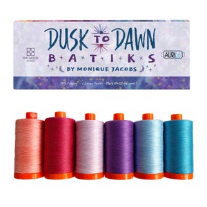 May include: A set of six large spools of 100% cotton thread in shades of peach, pink, lavender, purple, blue, and teal. The spools are labeled "Aurifil" and are part of the "Dusk to Dawn Batiks by Monique Jacobs" collection.