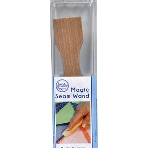 May include: A wooden seam pressing tool called "Magic Seam Wand" by June Tailor. The tool is in a clear plastic package with a blue and white label. The label shows a hand using the tool to press fabric seams. The label also says "Perfectly press seam allowances."