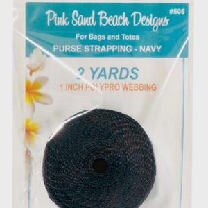 May include: A roll of navy blue 1 inch polypro webbing for bags and totes, packaged in a clear plastic bag labeled Pink Sand Beach Designs #505. The label specifies 2 yards of material and features a floral graphic on the left side.