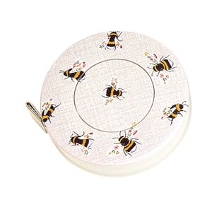 May include: A circular tape measure with a bee and floral design. The tape measure is off-white with a metal clip and a white border. The bees are black and yellow with floral details. A practical tool for measuring in sewing and craft projects.