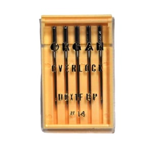 Może przedstawiać: Opakowanie igieł do maszyny do szycia overlock Organ. Igły są czarne ze srebrnymi końcówkami, ułożone pionowo w przezroczystym plastikowym etui z żółtą ramką. Na etui wydrukowano tekst "ORGAN OVERLOCK DCX1F BP #14".