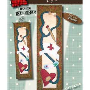Könnte beinhalten: Ein Quiltmuster für einen Wandbehang mit dem Titel "Nursing" mit einem Stethoskop, einer Krankenschwestermütze, Verbänden und einem Herzen. Das Muster ist 15 cm x 48 cm groß und beinhaltet einen Aufhänger. Der Schwierigkeitsgrad ist Anfänger. Der Text "Fertig in einem Tag!" steht auf dem Muster.