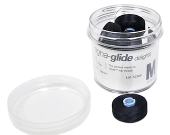 Może przedstawiać: Przezroczysty plastikowy pojemnik z czarną pokrywką wypełniony czarnymi szpulkami nici. Etykieta na pojemniku zawiera napis "agna-glide delights" i "The perfect match to Glide top thread." Etykieta zawiera również tekst "NAVY" i "Lot 123AF".