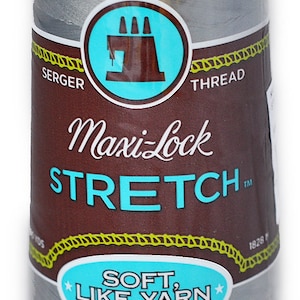Peut inclure: Une bobine de fil à coudre Maxi-Lock Stretch gris argenté. L'étiquette indique "Maxi-Lock Stretch" et "Soft, Like Yarn, Textured Nylon".