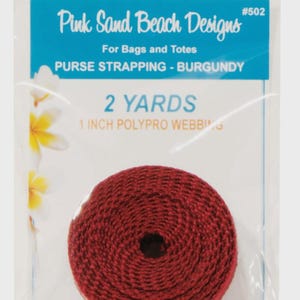 May include: A roll of burgundy 1 inch polypro webbing for bags and totes, labeled 2 yards, packaged in a clear plastic bag with Pink Sand Beach Designs #502 branding and a floral graphic on the left side of the white and blue header card.