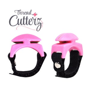 Pode incluir: Dois anéis cortadores de fio rosa com tiras ajustáveis pretas. Os anéis têm uma pequena lâmina na parte superior para cortar o fio.