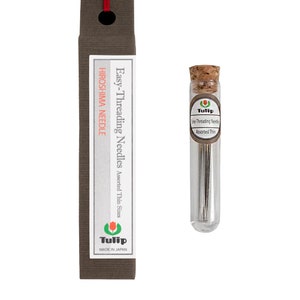 May include: A glass tube filled with assorted thin needles for sewing. The tube has a cork top and a label that reads "Tulip Easy-Threading Needles Assorted Thin". The tube is sitting on a brown cardboard box with the text "Tulip Easy-Threading Needles Assorted Thin Sizes Hiroshima Needle Made in Japan".