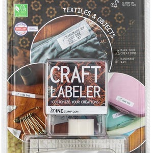 May include: A craft labeler kit with a clear plastic case, a white ink pad, a roll of white tape, and a set of alphabet and symbol stamps. The kit includes 20 dishwasher safe labels and 1 iron-on textile tape. The packaging features the text "CRAFT LABELER - CUSTOMIZE YOUR CREATIONS - MINE STAMP.COM".