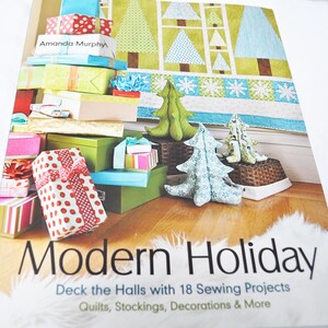 May include: A book titled Modern Holiday by Amanda Murphy featuring 18 sewing projects including quilts, stockings, and decorations. The cover displays a stack of colorful wrapped gift boxes and fabric Christmas trees on a wooden floor.