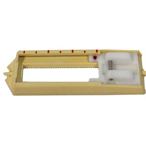 May include: A beige plastic sewing machine foot with a white plastic guide and a metal pin. The foot has a ruler with red markings.
