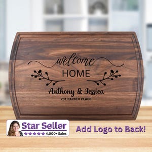 May include: A rectangular wooden chopping board with curved edges. The board is engraved with the words "welcome HOME" and the names "Anthony & Jessica" along with their address. Decorative floral elements are included.