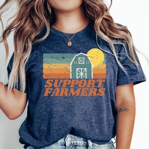 May include: A navy blue t-shirt with a vintage-style graphic of a barn, sun, and the text "SUPPORT FARMERS".